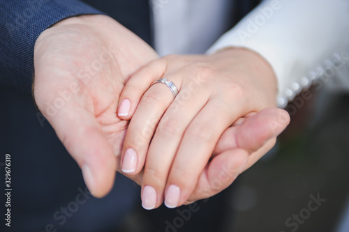 Close-up of groom's hand holding bride's hand tender. Hands of bride and groom with rings on wedding bouquet. Marriage concept.
