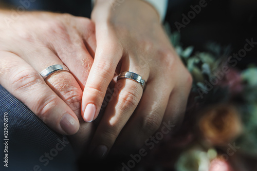 Close-up of groom s hand holding bride s hand tender. Hands of bride and groom with rings on wedding bouquet. Marriage concept.