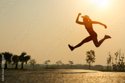 Silhouette, young woman sports jumping on road in the park while sunrise