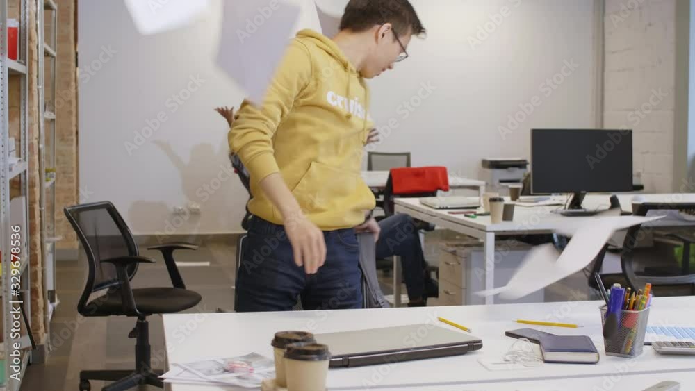 Joyous young multiethnic colleagues in casual clothes working at desks, throwing papers in the air, smiling and leaving office while celebrating business success Joyous young multiethnic colleagues in casual clothes working at desks, throwing papers in the air, smiling and leaving office while celebrating business success
