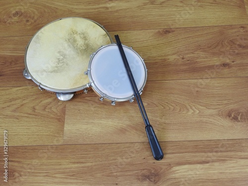 Two Brazilian percussion musical instruments: pandeiro (tambourine) and tamborim with drumstick, on a wooden surface. They are widely used in samba and pagode ensembles, popular Brazilian rhythms.
