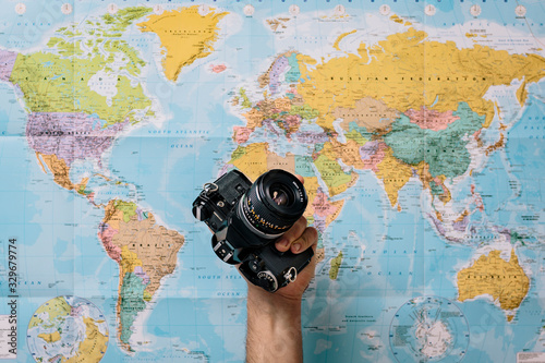 detail of a man's hand holding a photo camera with a world map in the background. Fun lifestyle concept while traveling.