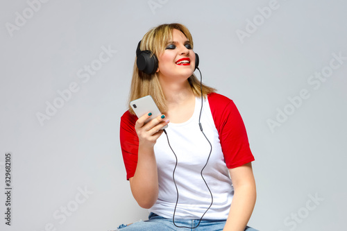 Portrait of Caucasian Girl In Casual Street Clothing Posing With Headphones And Smartphone Indoors. Against White.