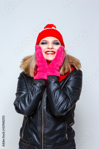 Portrait of Funny Caucasian Blond Girl In Warm Hat and Scarf Posing With Laughing Facial Expression Against White.