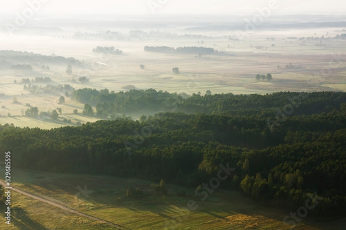 Morning sunrise balloon flight. Top view landscape. Foggy mystic forest and harvest fields. Panoramic scenery of Poland. Natural european environment background.