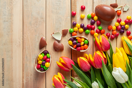 Beautiful red and yellow tulips for easter holiday. Chocolate eggs and candies on a wooden background.
