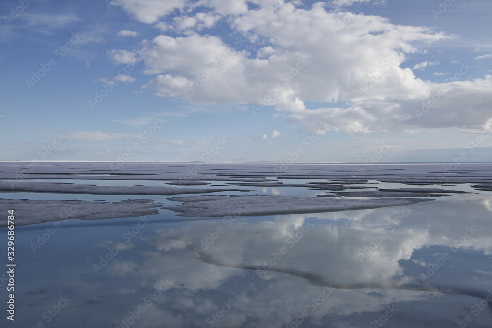 Broken pans of sea ice on ocean coast with blue sky and clouds along the Northwest Passage in June, Cambridge Bay, Nunavut