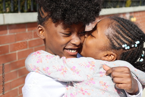 African American girls hugging near brick wall  outside on city street 