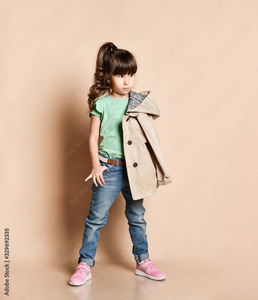 Cute girl posing standing in different poses, in jeans with belt, green t-shirt and beige coat and pink sneakers Cute girl posing standing in different poses, in jeans with belt, green t-shirt and beige coat and pink sneakers