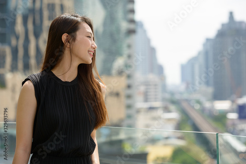 Happy young beautiful Asian businesswoman against view of the city