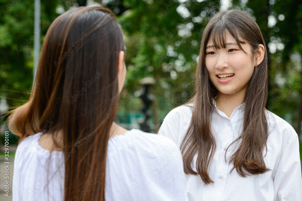 Two young beautiful Asian teenage girls talking at the park Two young beautiful Asian teenage girls talking at the park
