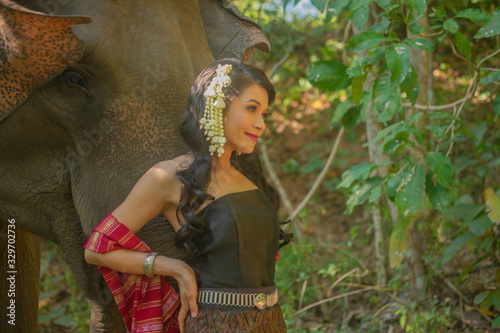 Beautiful thai women wearing traditional thai clothes standing on an elephant in nature park thailand, woman concept