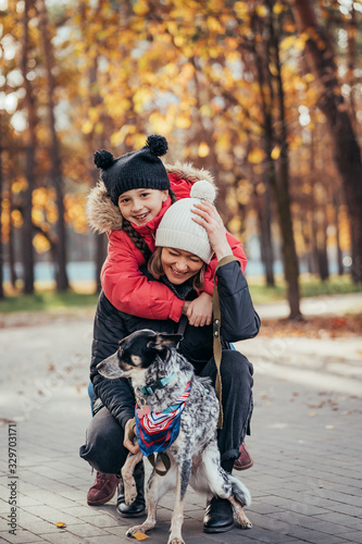 Happy mother and her daughter playing with dog in autumn park