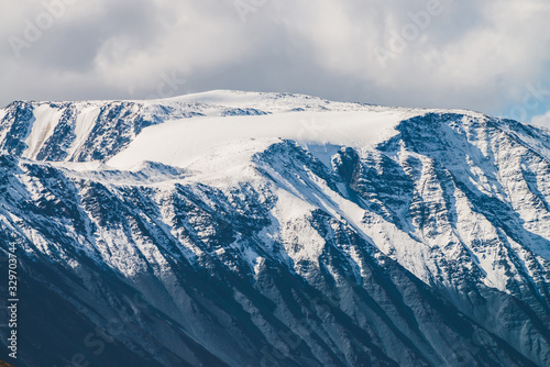 Atmospheric alpine landscape to snowy mountain ridge in sunny day. Snow shines in day light on mountain peak. Beautiful shiny snowy top. Wonderful scenery to low clouds above range covered with snow. © Daniil