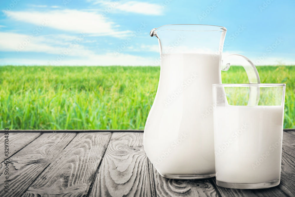 Pitcher and glass of milk on wooden table in field Pitcher and glass of milk on wooden table in field