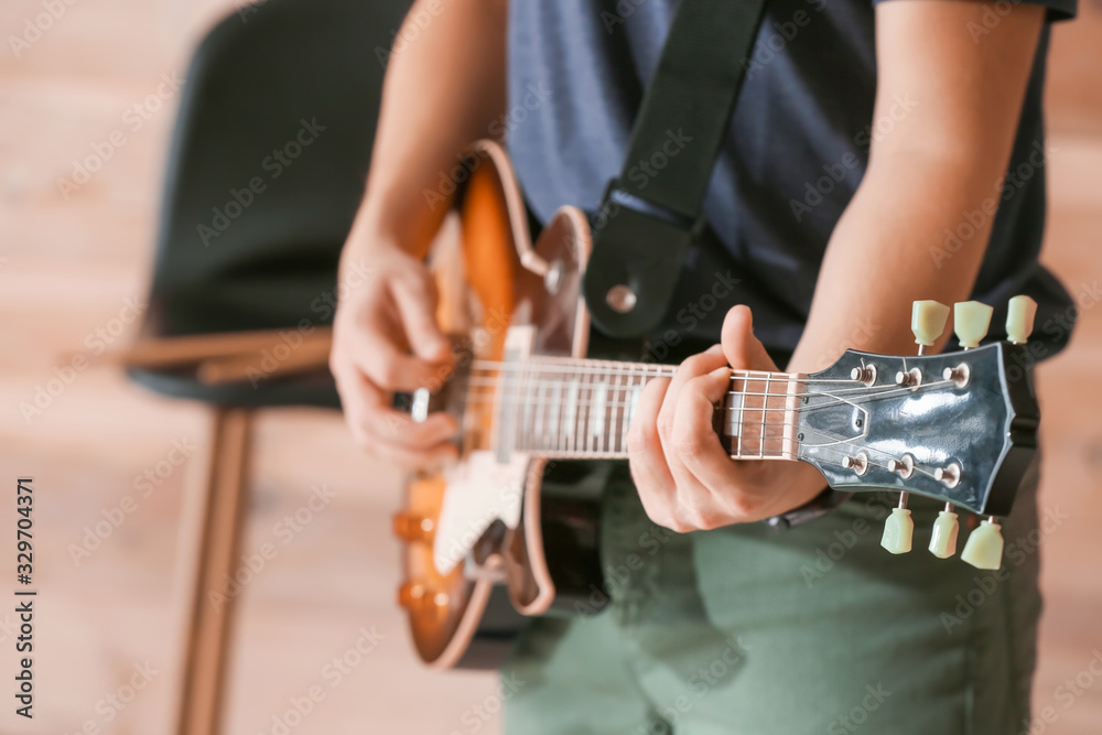 Young man playing guitar near wooden wall, closeup