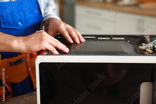 Worker repairing microwave oven in kitchen, closeup © Pixel-Shot