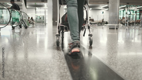 Woman Carry Luggage Cart Walk at Airport Terminal. Tracking Shot of Girl Legs in Trainers. Female Traveler Pushing Trolley with Baggage Forward to Boarding Gate. © Goinyk