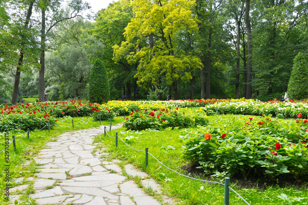 Saint Petersburg. People walk in a beautiful city park with flower beds and relax on benches in the shade of green trees on Elagin Island