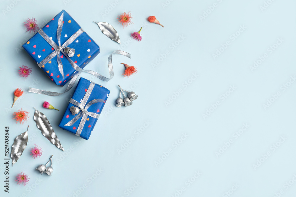 Gifts wrapped in blue hearts paper and tired with silver ribbon. Silver painted eucalyptus leaves and gum nuts, plus flowering gum nuts surround the presents on a blue background.. Gifts wrapped in blue hearts paper and tired with silver ribbon. Silver painted eucalyptus leaves and gum nuts, plus flowering gum nuts surround the presents on a blue background..