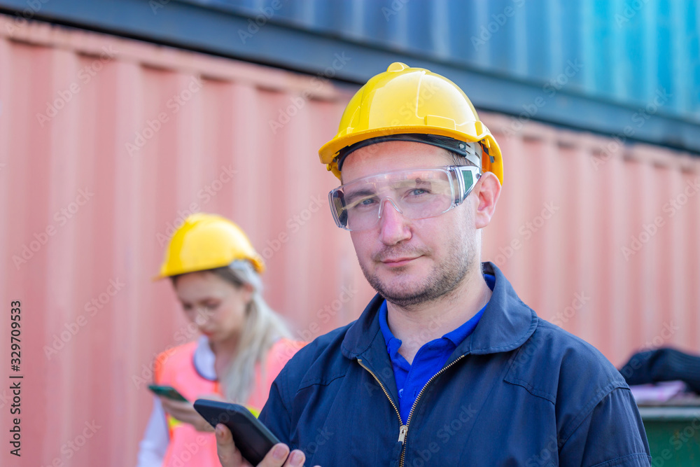 Engineer in the hard hat uses mobile phone, Industrial worker using mobile smartphone in industry containers cargo Engineer in the hard hat uses mobile phone, Industrial worker using mobile smartphone in industry containers cargo
