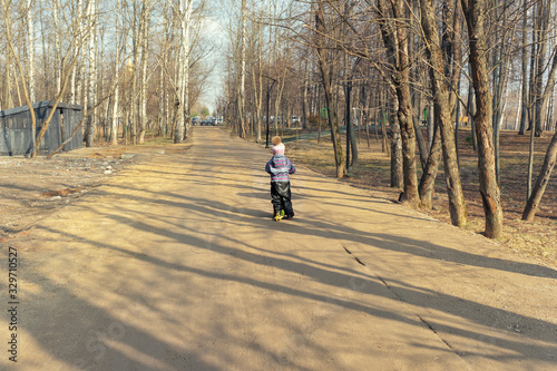 child 4 years old rides a yellow scooter on a dirt road in a city park