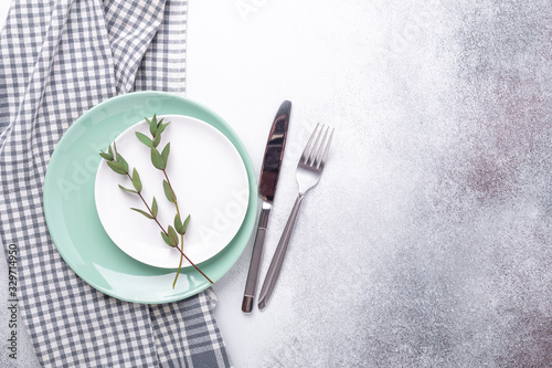 Empty mint and white plates, linen napkin, eucalyptus leaves and cutlery on stone background Copy space Top view