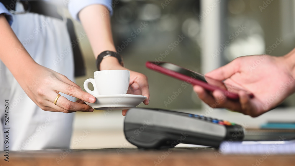 Cropped image of smart man's hands holding a smartphone and doing a payment by using a NFC technology at the Credit card reader that putting on cafe payment counter. Technology and Payment concept.