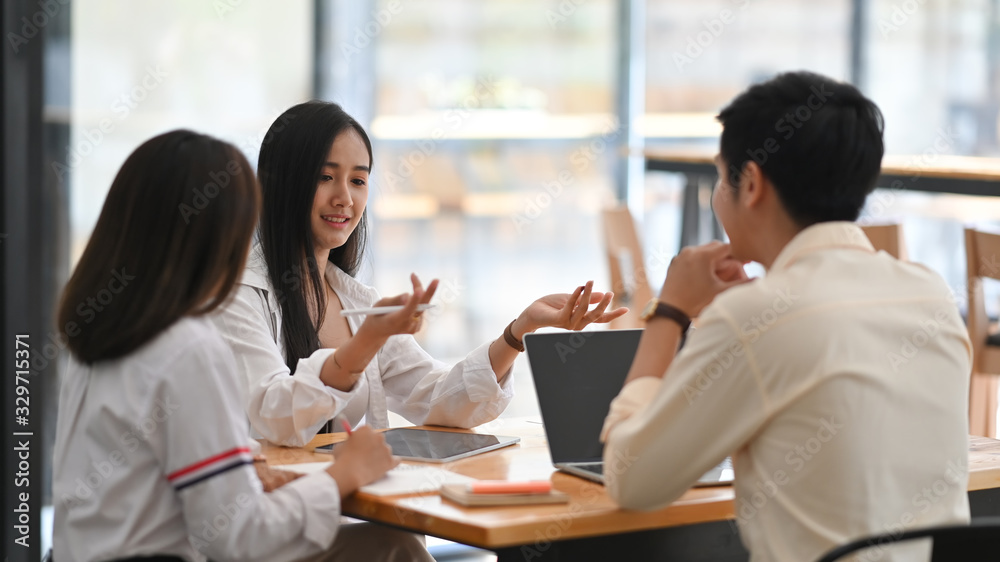 Photo of business development team discussing/talking/meeting/briefing together while sitting at the wooden meeting table with modern office as background. Photo of business development team discussing/talking/meeting/briefing together while sitting at the wooden meeting table with modern office as background.