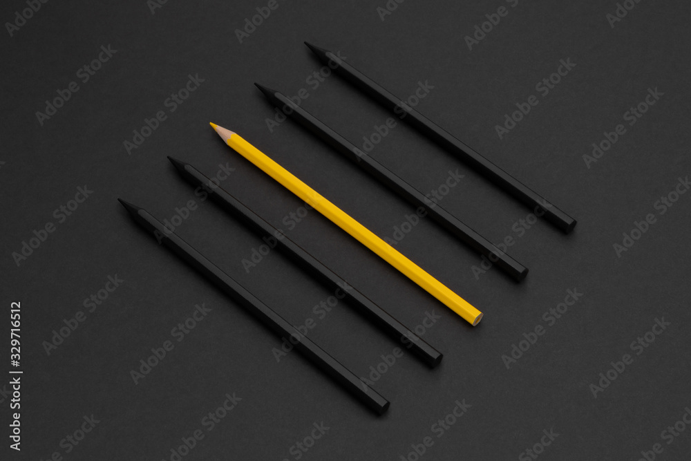 Yellow pencil among black pencils on the matte black background ...