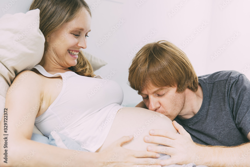 Happy young couple expecting baby. Man kissing baby bump. Happy expectant parents concept Happy young couple expecting baby. Man kissing baby bump. Happy expectant parents concept