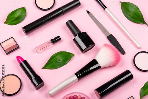 Various cosmetic accessories for makeup and manicure on a trendy pastel pink background with fresh green leaves. Blush, brush, eye shadow, mascara, perfume, lipstick, nail Polish. Skin care products.