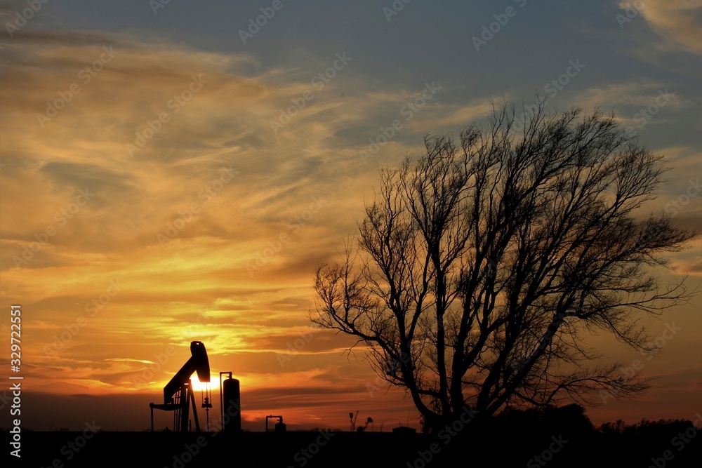 Silhouette of a tree and Oilwell Pump with a colorful Sunset.