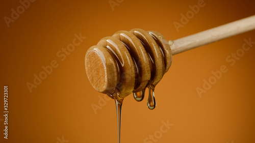 Honey dripping from honey dipper. Thick honey dipping from the wooden honey spoon. yellow background. closeup