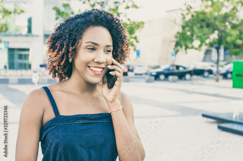 Happy cheerful woman excited with phone talk. Young black woman walking down city street, talking on mobile phone, smiling, laughing. Communication or good news concept