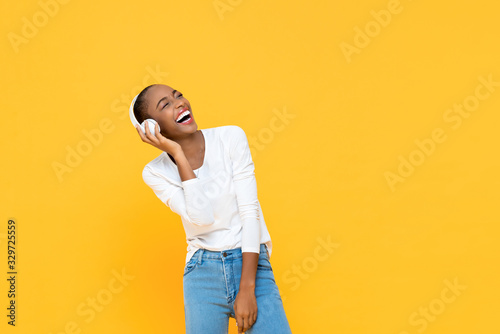 Happy African American woman laughing while listening to music on wireless headphone isolated on yellow background