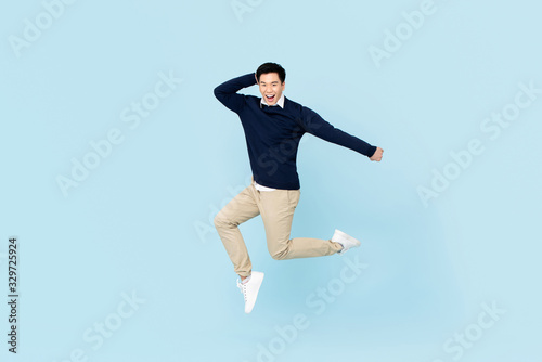 Smiling young handsome Asian man jumping on light blue studio background