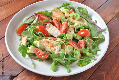 Chicken salad with avocado and cherry tomatoes, arugula and beet leaves. Healthy lunch bowl with vegetables and chicken on a wooden background. Healthy food concept