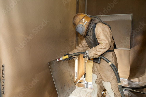Photos Man in protective clothing cleans industrially with high-pressure sandblasting