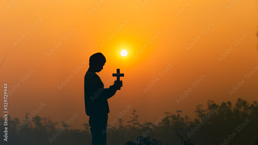 human holding christian cross and praying in morning light, christian silhouette concept.