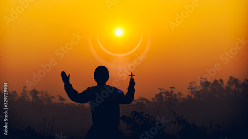 human holding christian cross and praying at sunset background. christian silhouette concept.