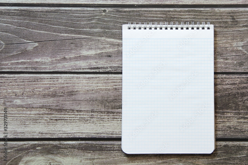 Notepad with a blank white sheet in a checker paper lies on the background of wooden boards Notepad with a blank white sheet in a checker paper lies on the background of wooden boards