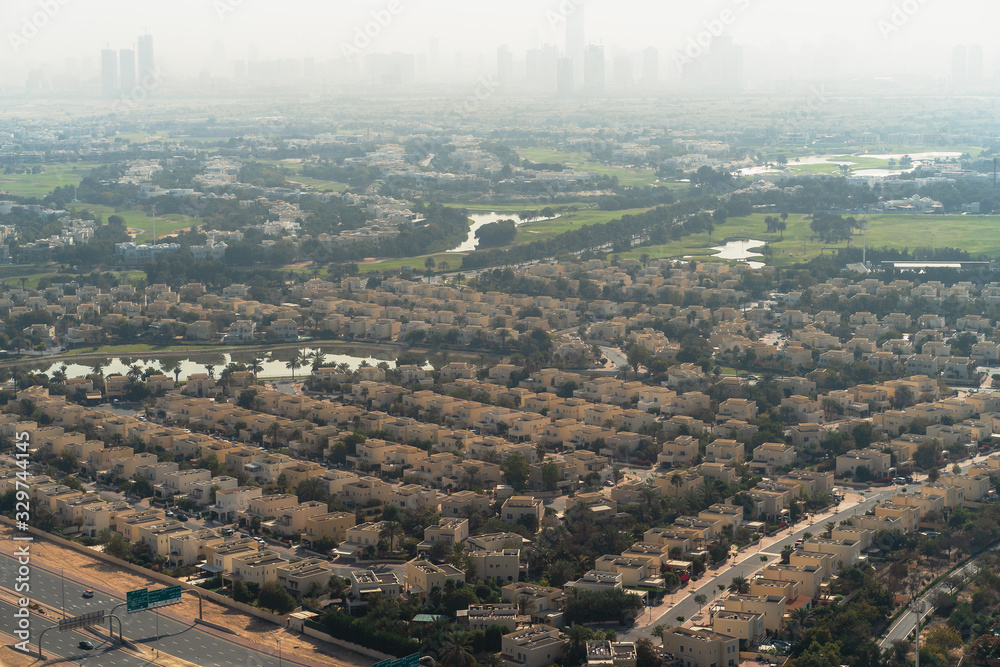 Aerial view of Dubai with villas and houses of local residents on foreground and high-rise skyscrapers buildings in morning dusk on background, United Arab Emirates.