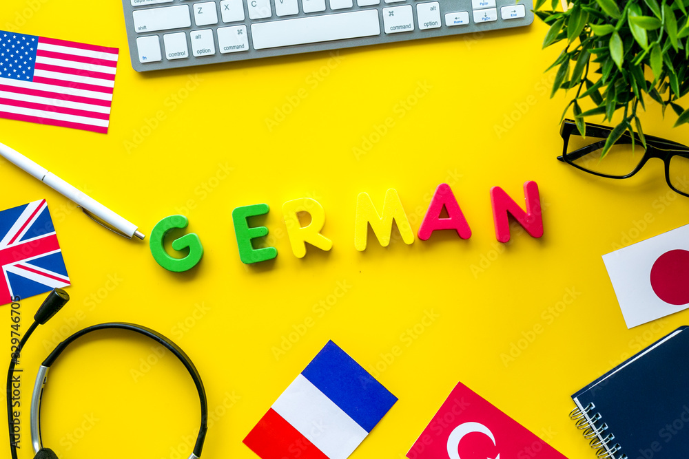 Learn German online. Concept with text, headset and keyboard on yellow background top-down
