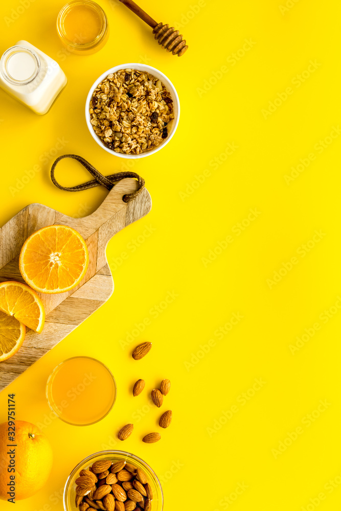 Morning granola near toast and oranges on yellow background top-down frame copy space