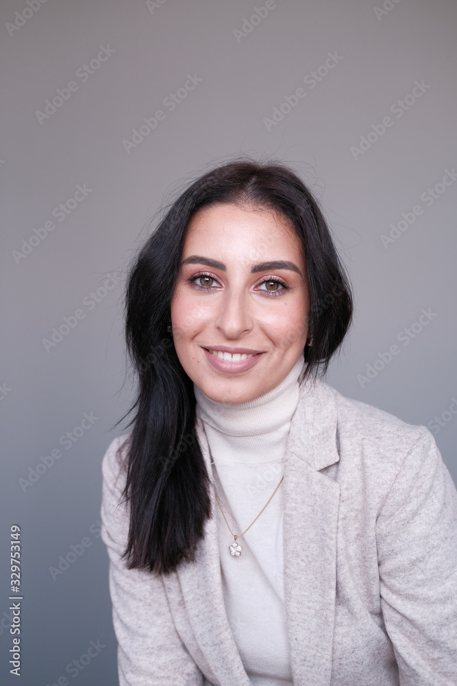 Portrait of a smiling mid-aged business woman in a light milk-colored trouser suit and turtleneck against a light wall.