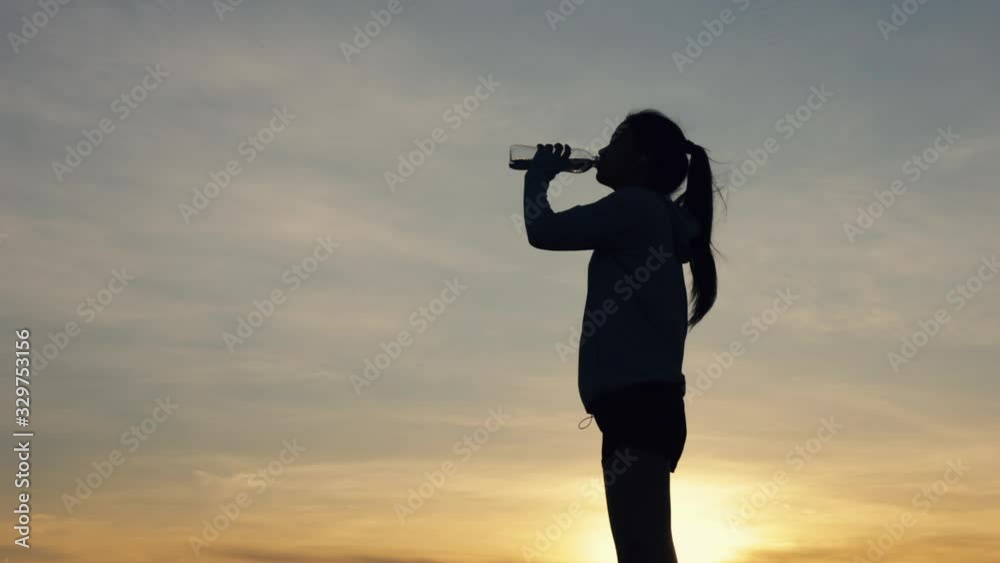 Silhouette athlete female runner drinking water after running fitness workout at the beach in the last sunlight. Healthcare lifestyle concept. Silhouette athlete female runner drinking water after running fitness workout at the beach in the last sunlight. Healthcare lifestyle concept.