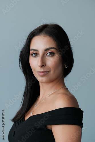 A large portrait of a middle-aged woman (30-35 years old) with dark hair and brown eyes in a black dress on a light background.