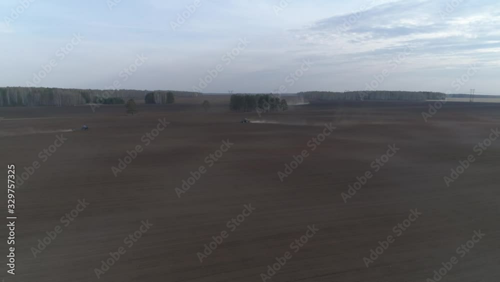 Two tractors plow in a huge field. Spring, evening Two tractors plow in a huge field. Spring, evening