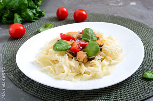 Pasta with mussels, tomatoes on a white plate on a wooden background photo